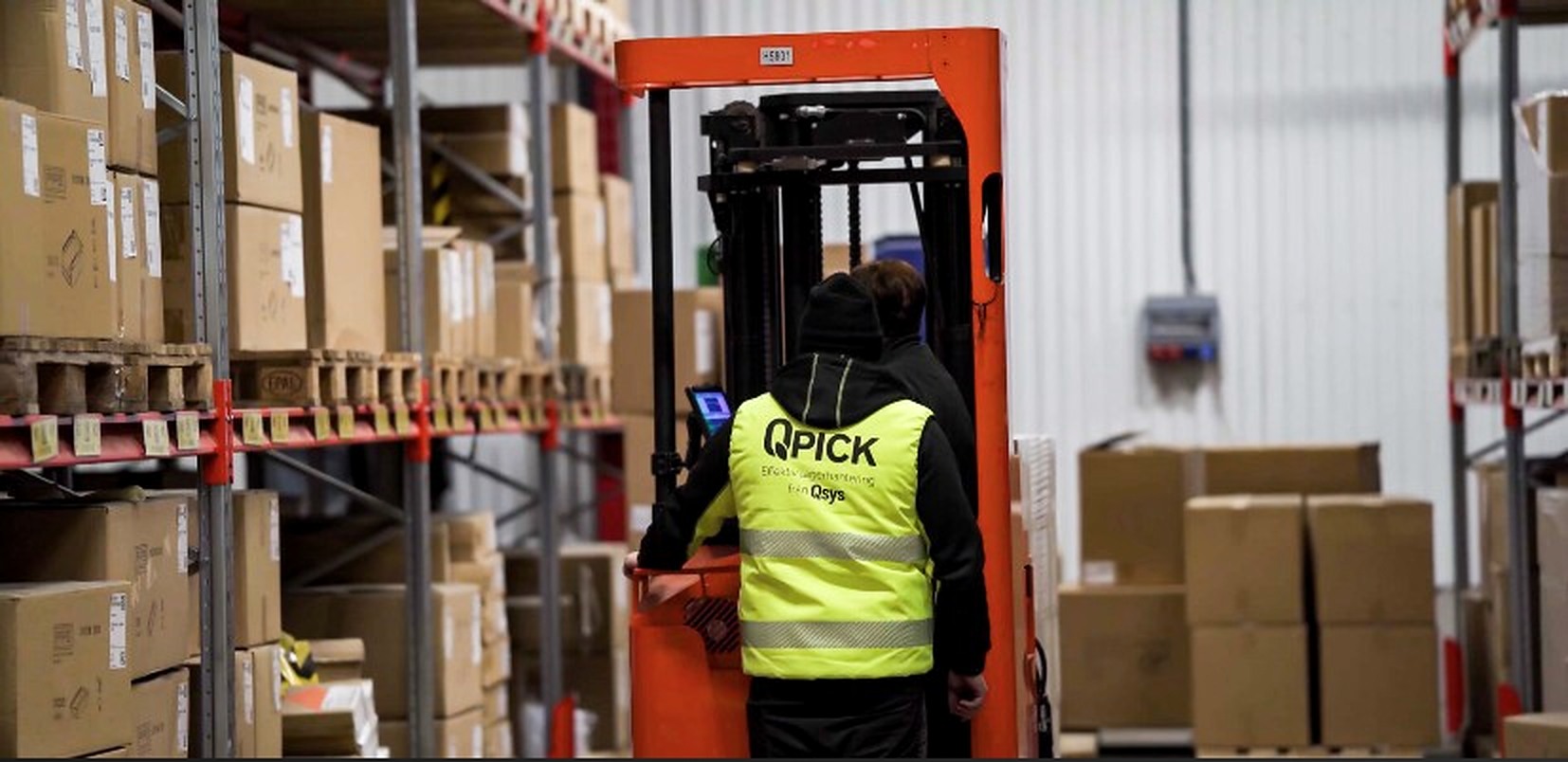 Lagermedarbetare i Qpick-väst vid truck i lager